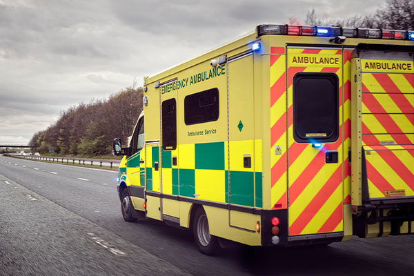 ambulance-driving-down-highway-with-flashing-lights-on-a-cloudy-day-to-show-quick-emergency-response-thanks-to-synergemnet-ng911-technology-including-i3-route