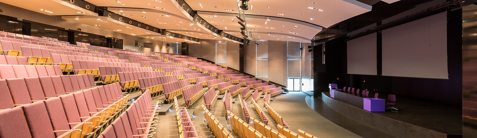 conference-hall-where-NENA-i3-standards-breakout-session-on-next-generation-9-1-1-will-be-held-currently-empty-with-auditorium-like-seats-and-stage-at-the-front-for-speaker